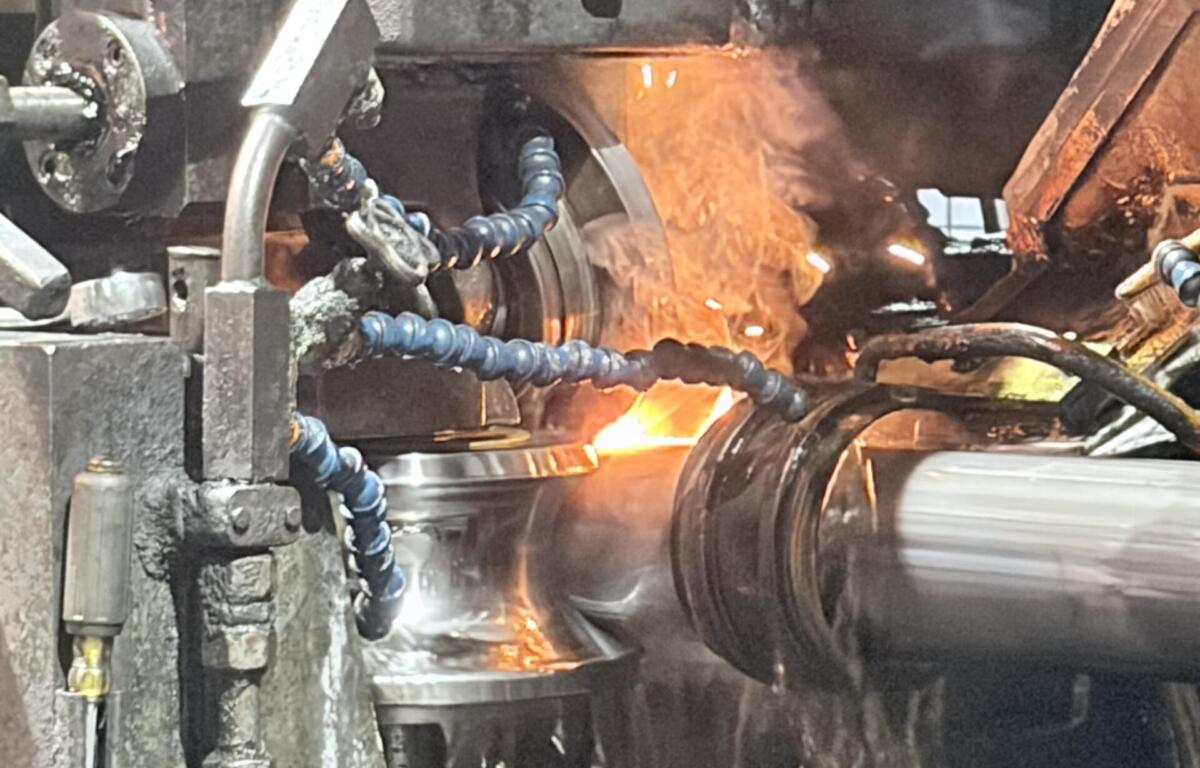 Close-up of a metalworking forge: molten metal glowing as a workpiece is processed, with sparks and industrial machinery around it