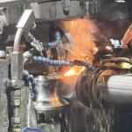 Close-up of a metalworking forge: molten metal glowing as a workpiece is processed, with sparks and industrial machinery around it