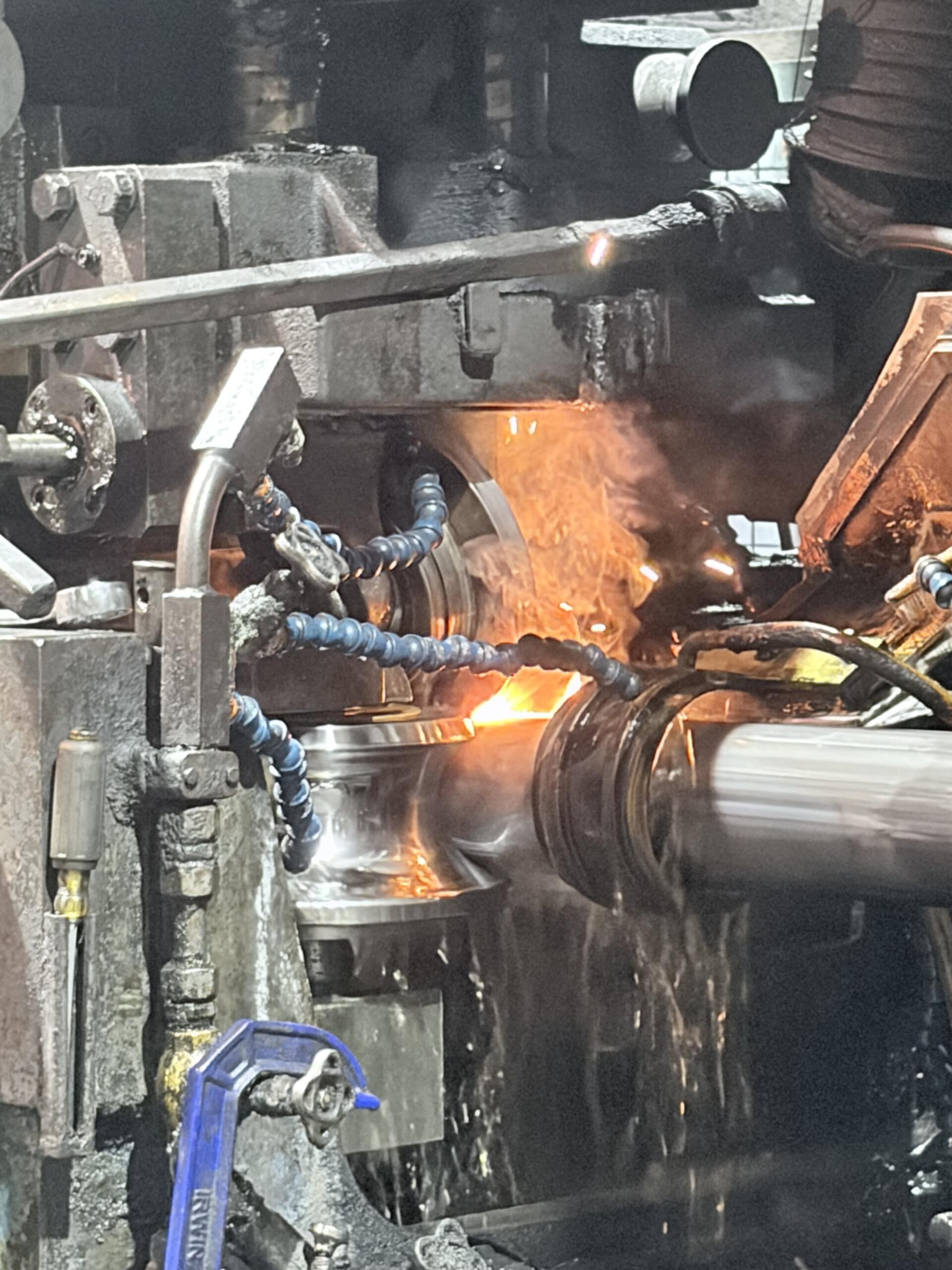 Close-up of a metalworking forge: molten metal glowing as a workpiece is processed, with sparks and industrial machinery around it