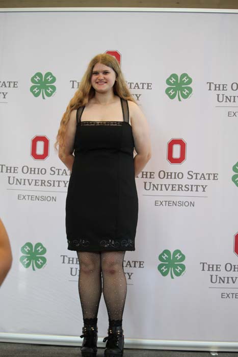 Young woman in a black dress posing on stage in front of an Ohio State University backdrop.