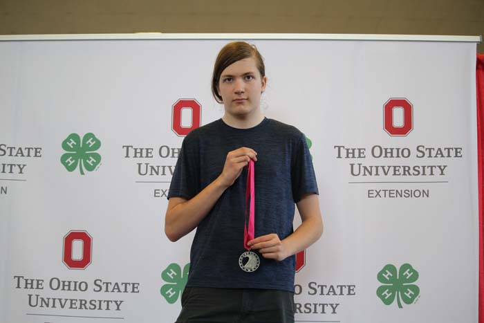 Person stands with a pink-ribbon medal in front of an Ohio State University Extension backdrop.