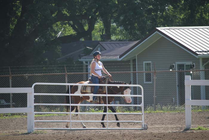 Rider wearing a helmet on a white-and-brown horse inside a fenced outdoor riding arena.