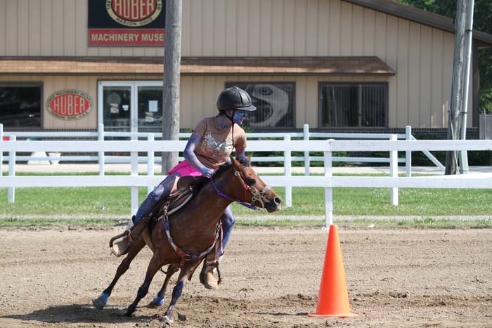 Rider in helmet guiding a brown horse around an orange cone in a dirt arena.