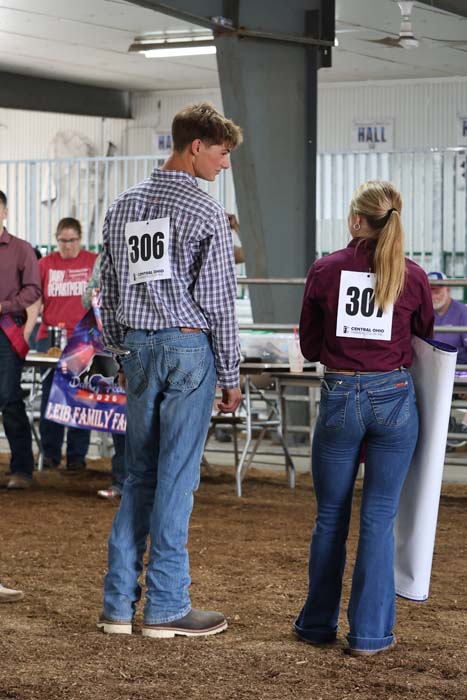 Two participants with race bibs on their backs stand with their backs to the camera at an indoor event.