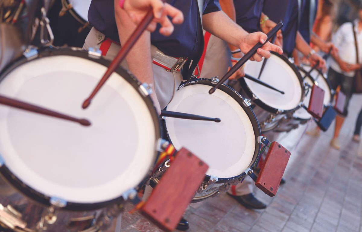 Row of street drummers in a parade, hitting white drumheads with sticks and mallets in motion