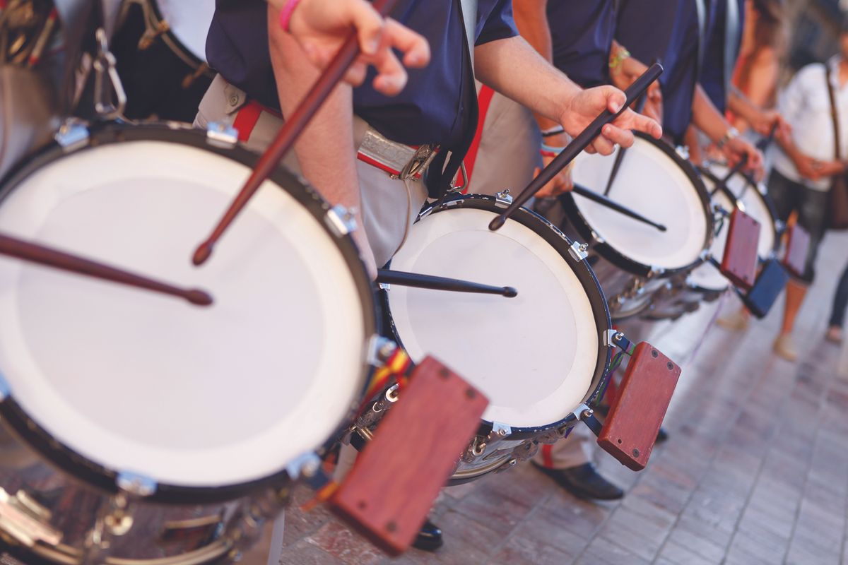 Row of street drummers in a parade, hitting white drumheads with sticks and mallets in motion