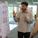 Man explains a scientific poster about cancer-related mutations to a woman at a conference or poster session.