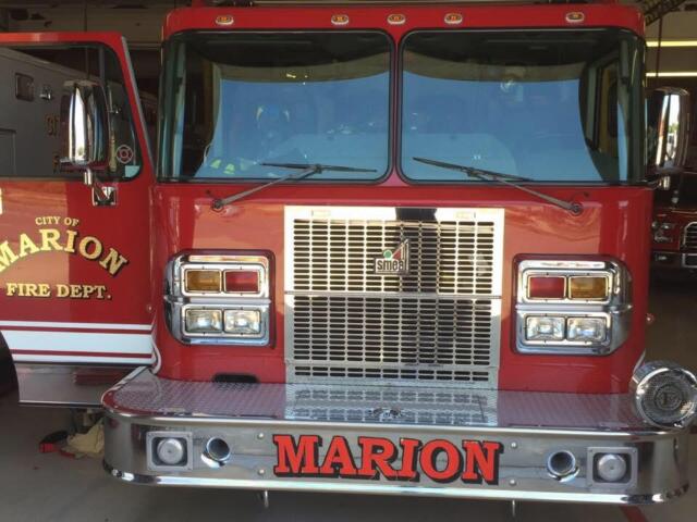 Front view of a red Marion Fire Department fire engine inside a station, with chrome bumper, large grille, and 'MARION' on the bumper area.