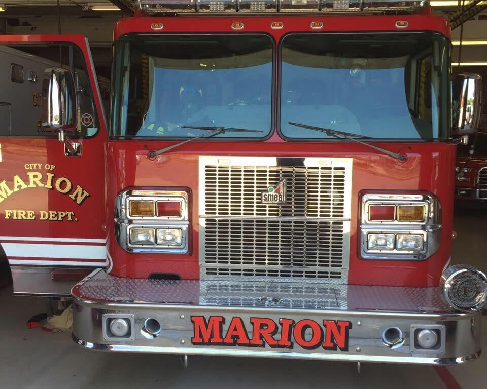 Front view of a red Marion Fire Department fire engine inside a station, with chrome bumper, large grille, and 'MARION' on the bumper area.