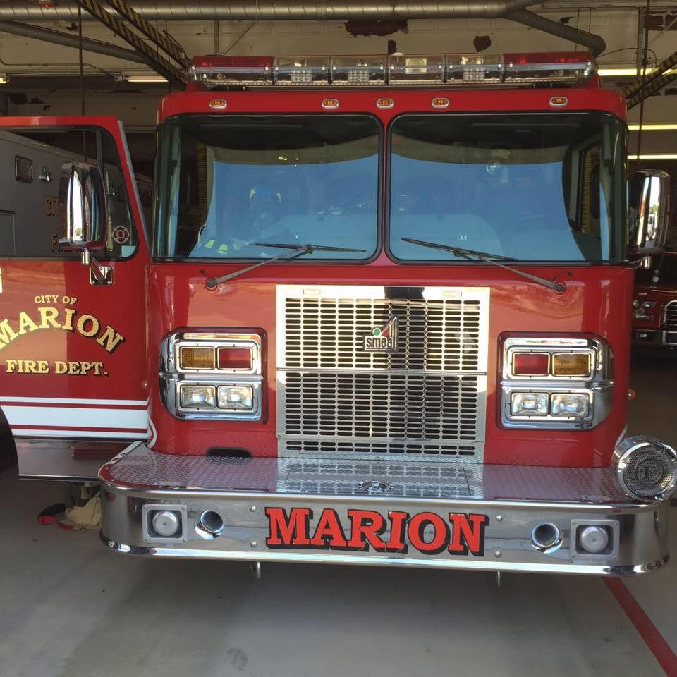 Front view of a red Marion Fire Department fire engine inside a station, with chrome bumper, large grille, and 'MARION' on the bumper area.
