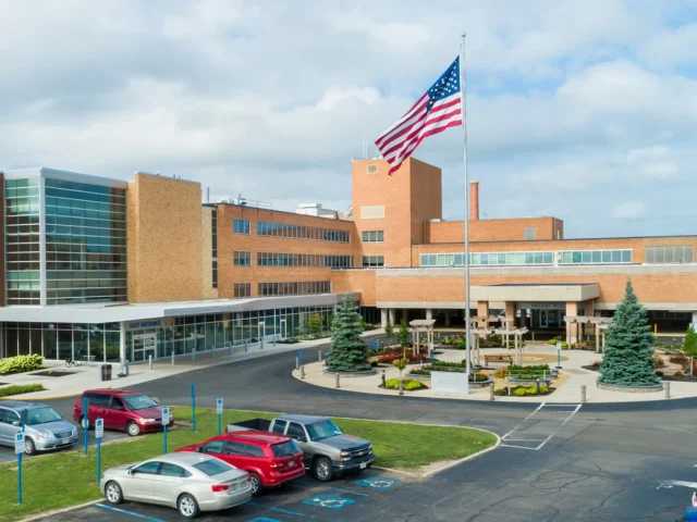 Exterior view of Marion General Hospital campus with a tall American flag, brick buildings, and a circular driveway with parked cars.