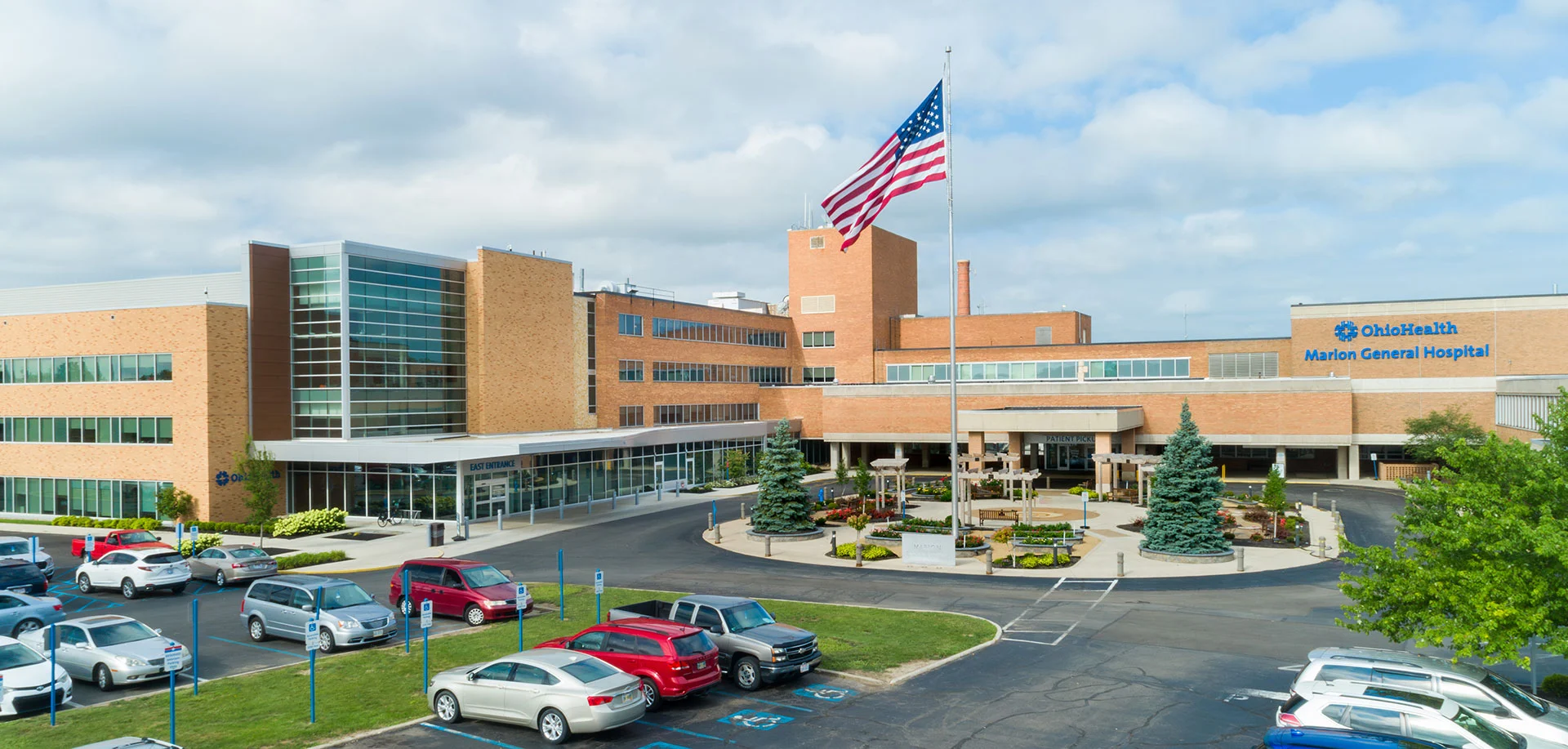 Exterior view of Marion General Hospital campus with a tall American flag, brick buildings, and a circular driveway with parked cars.