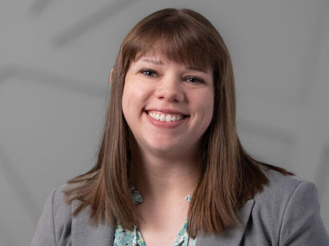 Smiling woman with shoulder-length brown hair wearing a gray blazer, facing the camera.
